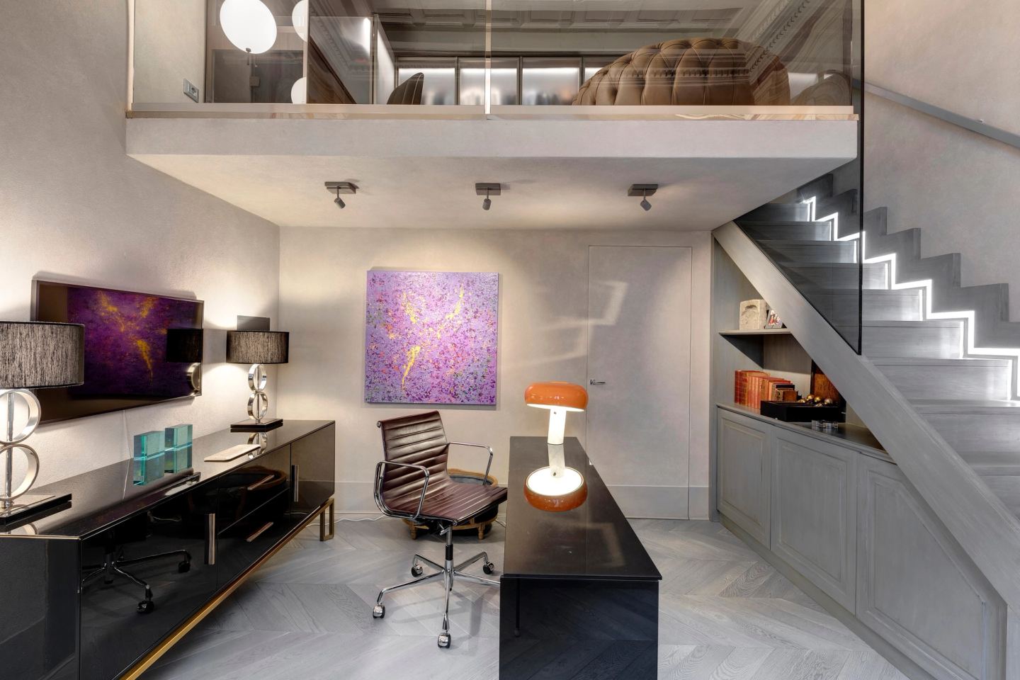 The home office under the mezzanine: a black desk and sideboard, the stair lit tread by tread