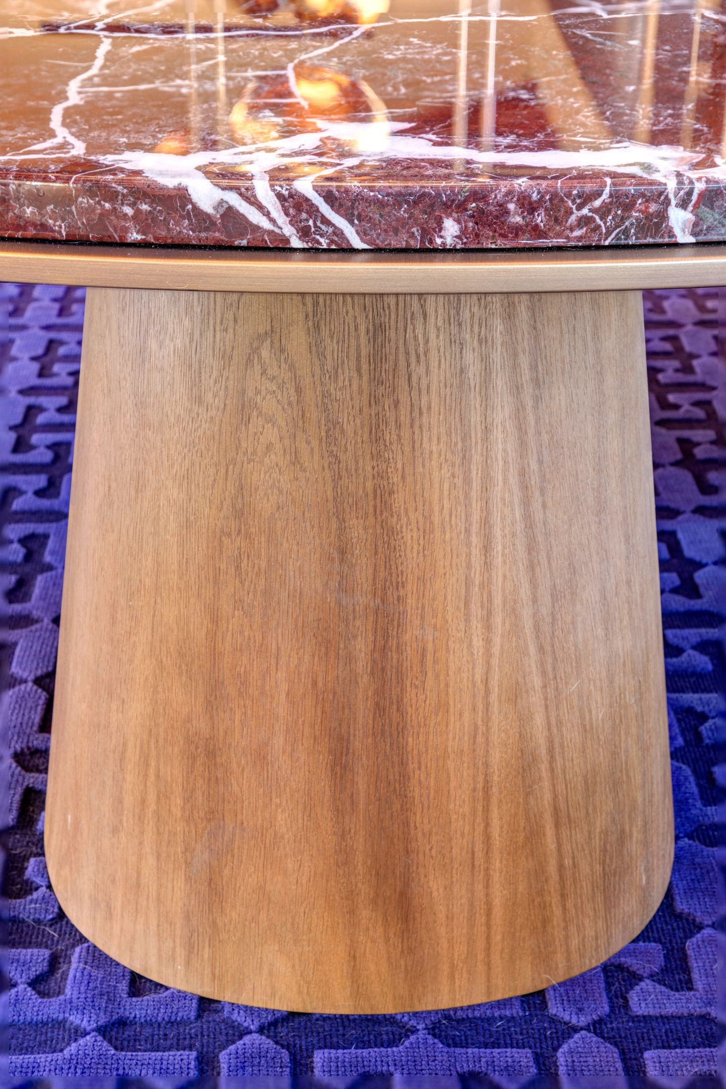 La base conica in legno del tavolo in marmo rosso sul tappeto blu