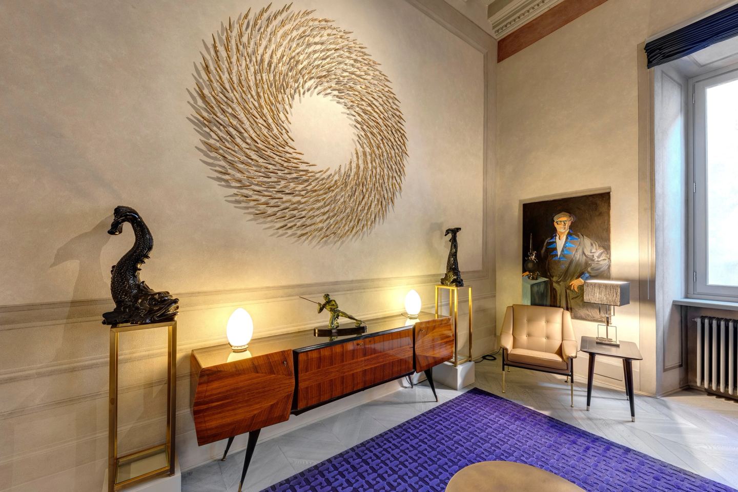 A spiral of gold on the wall above a wooden sideboard, two dark dolphin sculptures on plinths