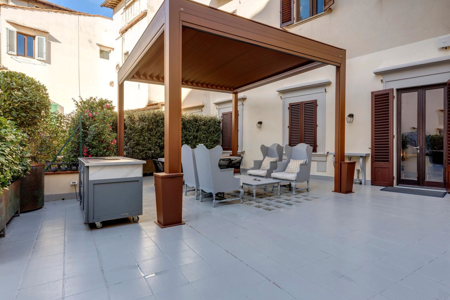 La pergola dall'altro lato della terrazza, un carrello grigio su ruote accanto, le porte dell'appartamento alle spalle