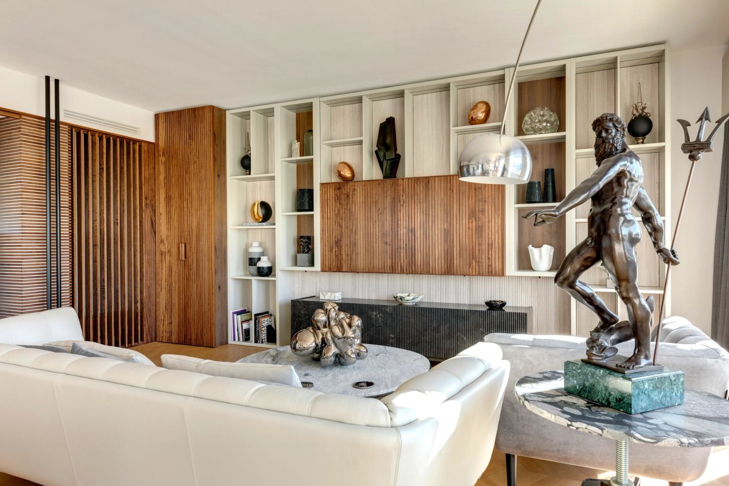 White sofa below the bronze figure, joinery wall of walnut and painted shelving behind