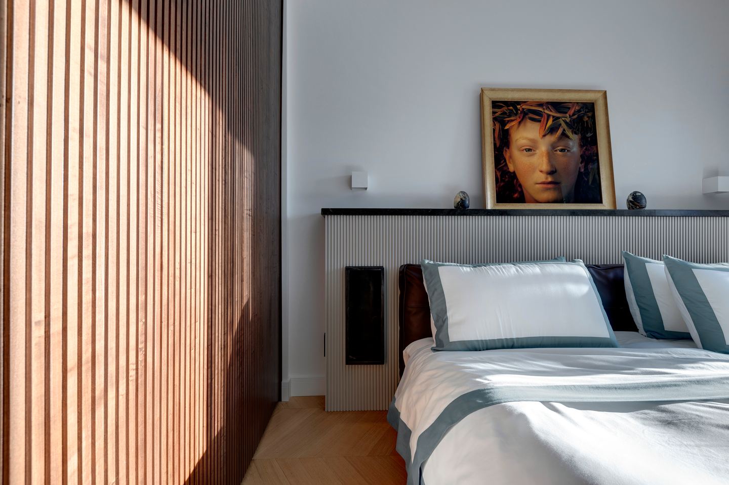 Raking light across the walnut slats beside the bed