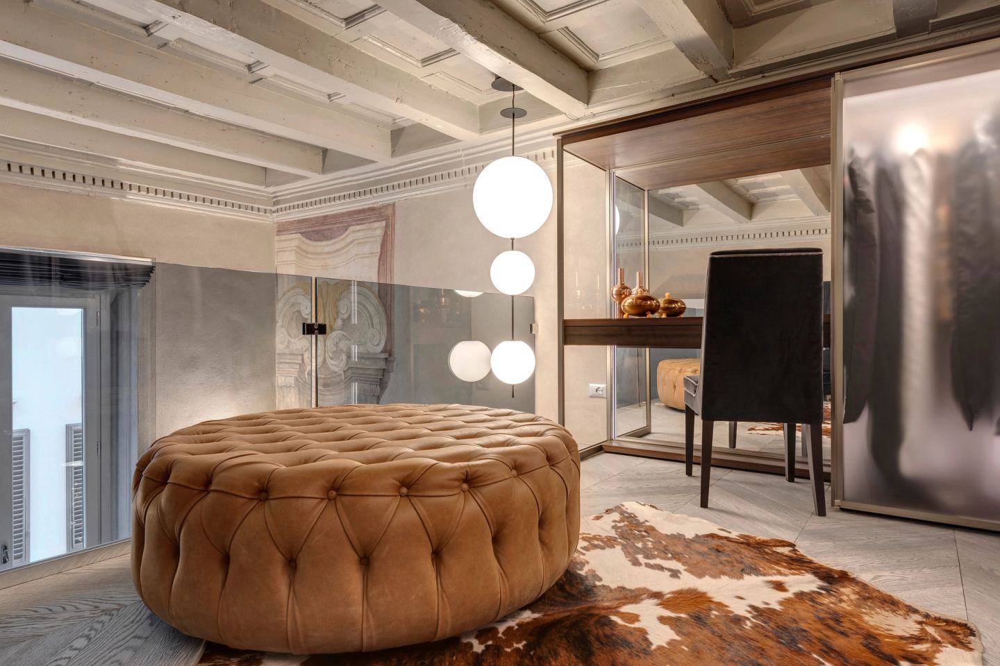 Un pouf tondo in pelle capitonné su una pelle bovina, la vanity e il parapetto in vetro alle spalle