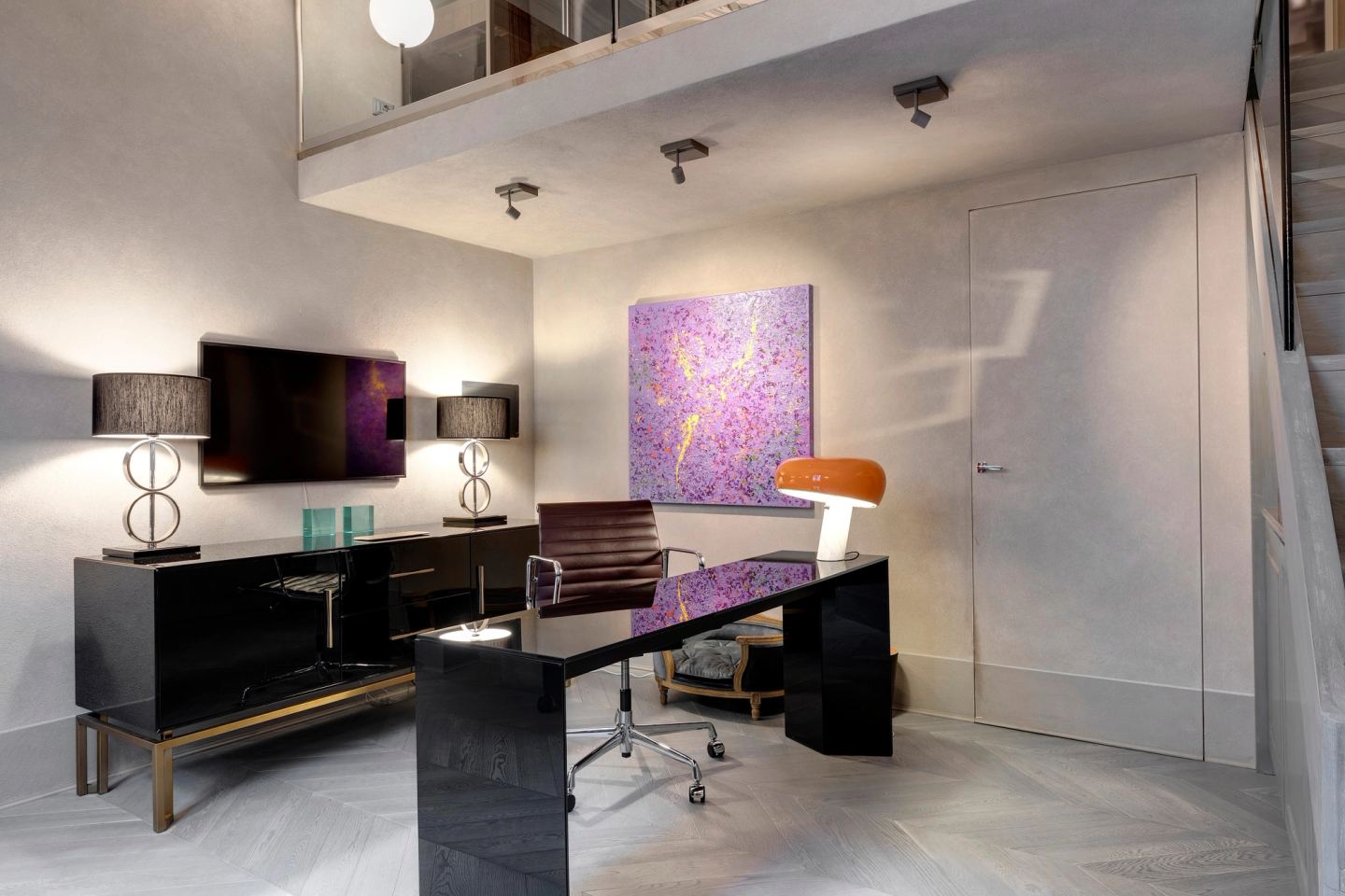 La scrivania con la sua lampada arancione, un quadro viola alla parete e una porta filo muro