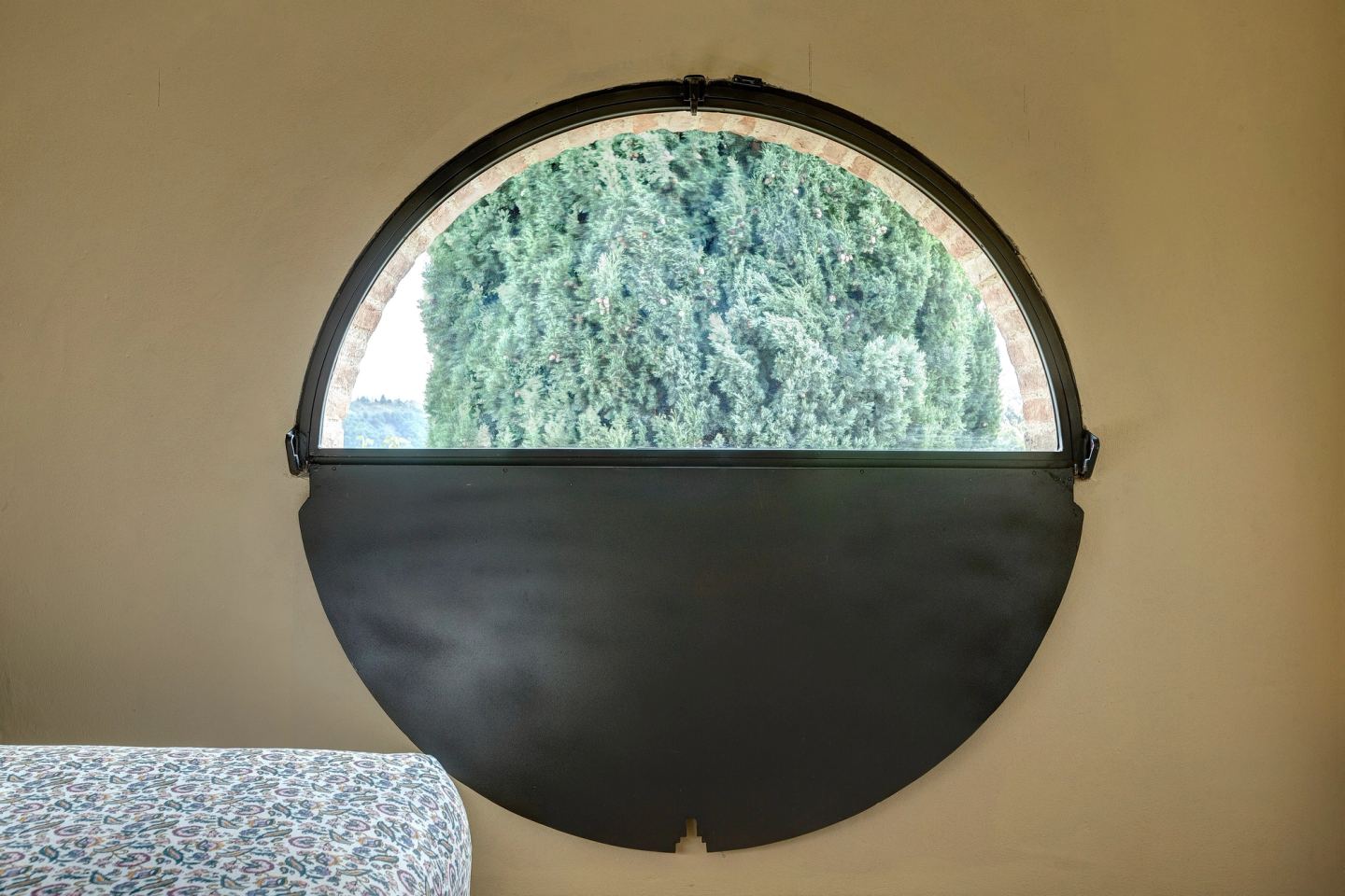 The round window, half glazed, half dark iron, cypresses outside