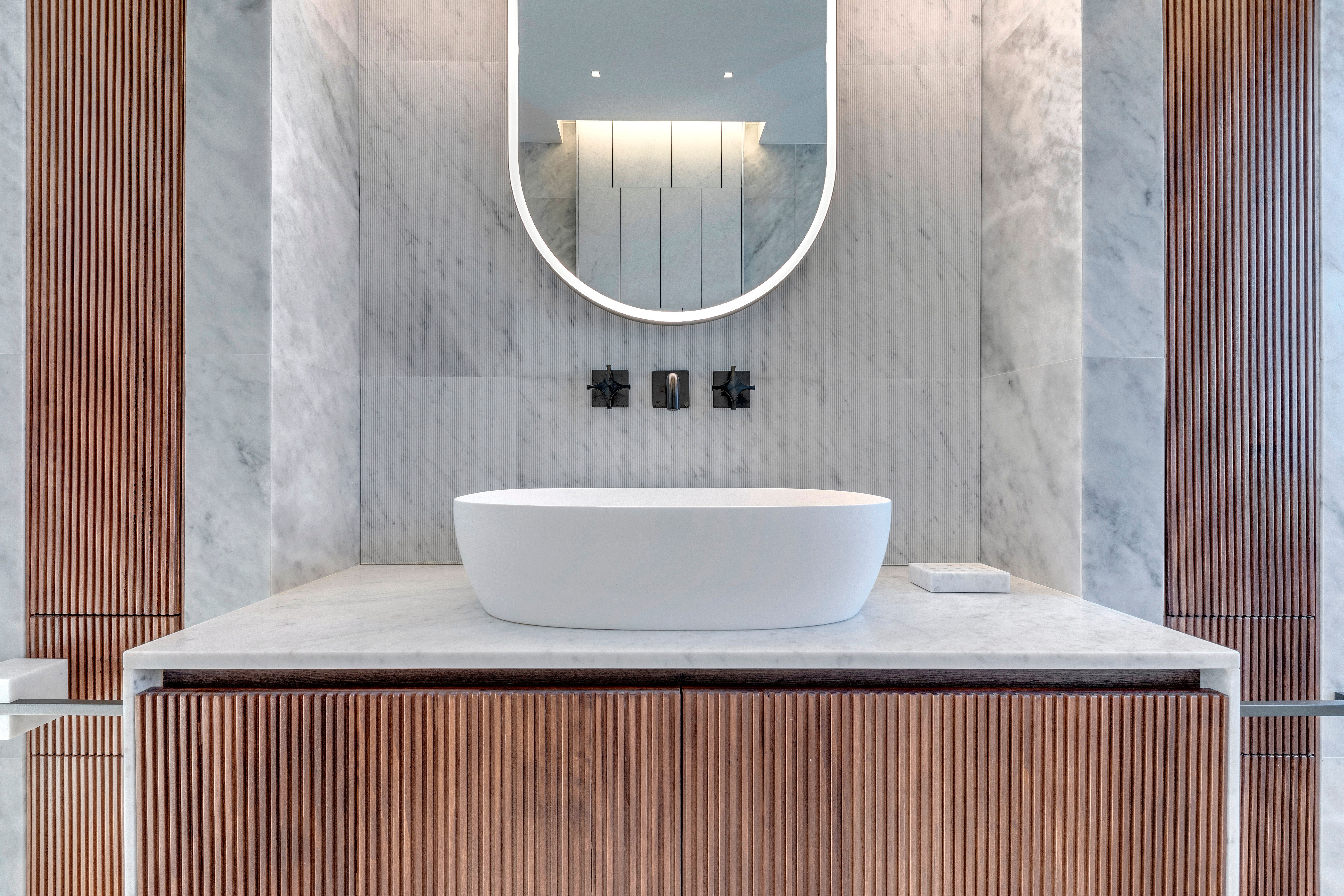 Fluted walnut vanity beneath the backlit oval mirror