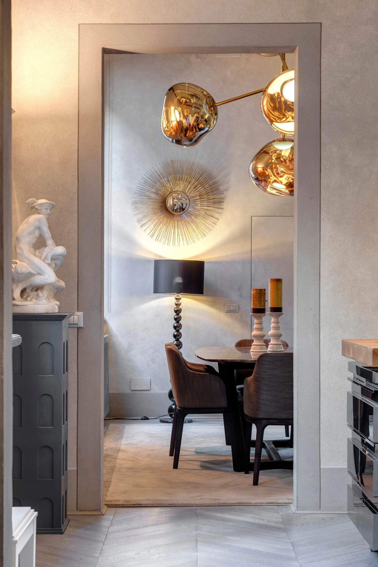 The dining room framed by a doorway, the chandelier and a sunburst wall light