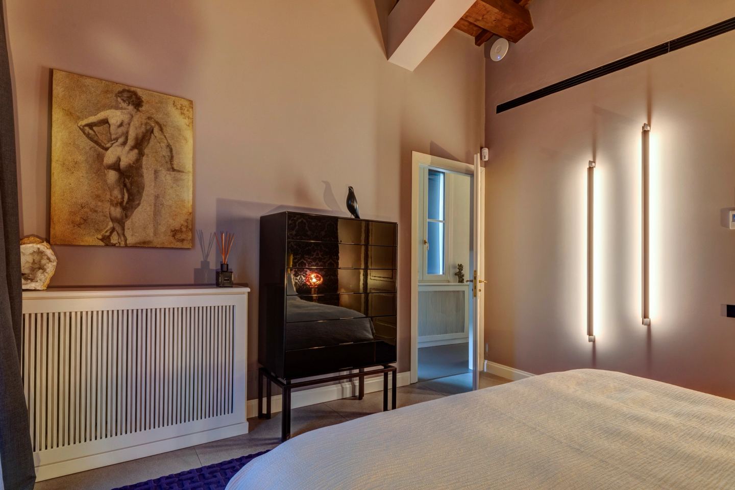 The far wall of the bedroom: a drawing above the panelled radiator cover, dark cabinet alongside