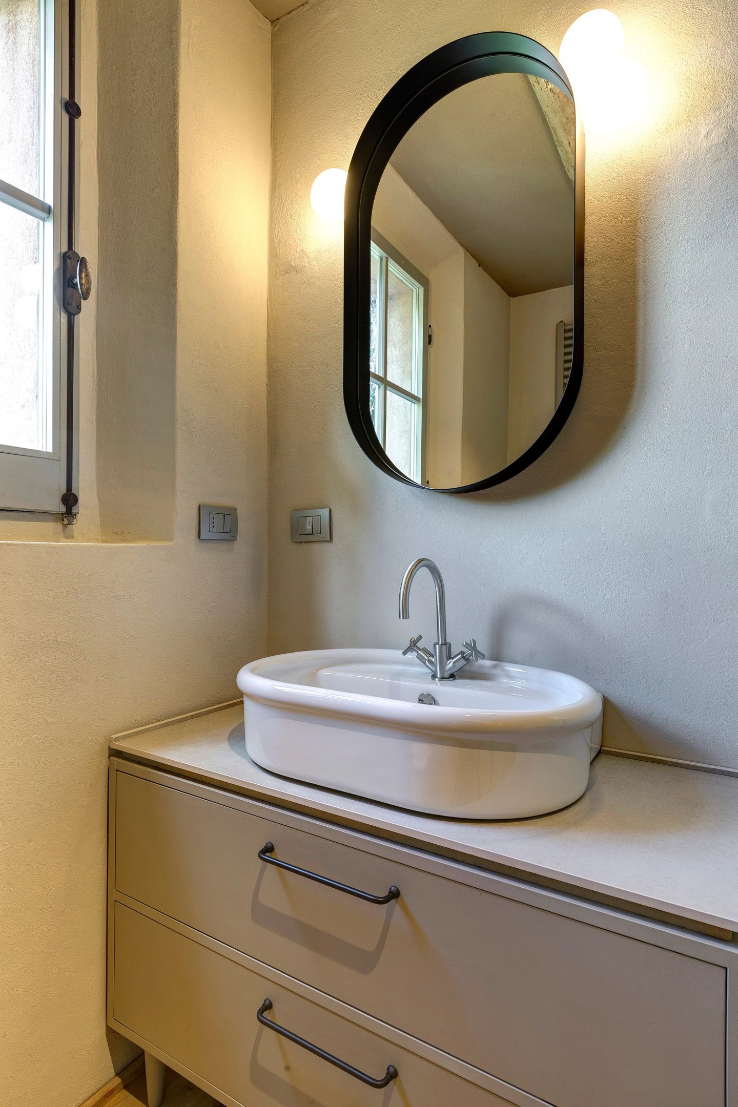 The basin on its made-to-measure cabinet, a black oval mirror above