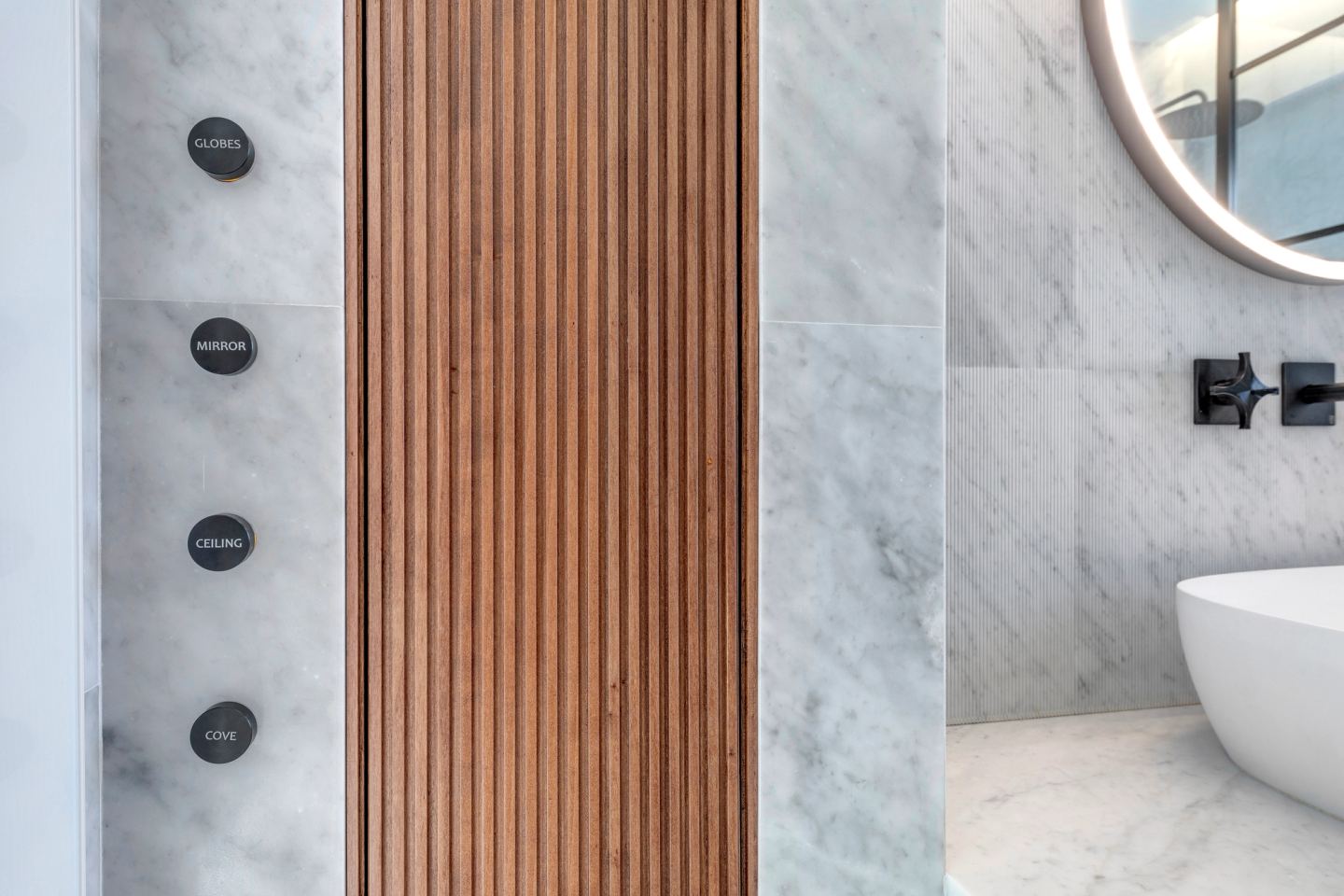 Engraved shower controls on the marble beside the fluted walnut