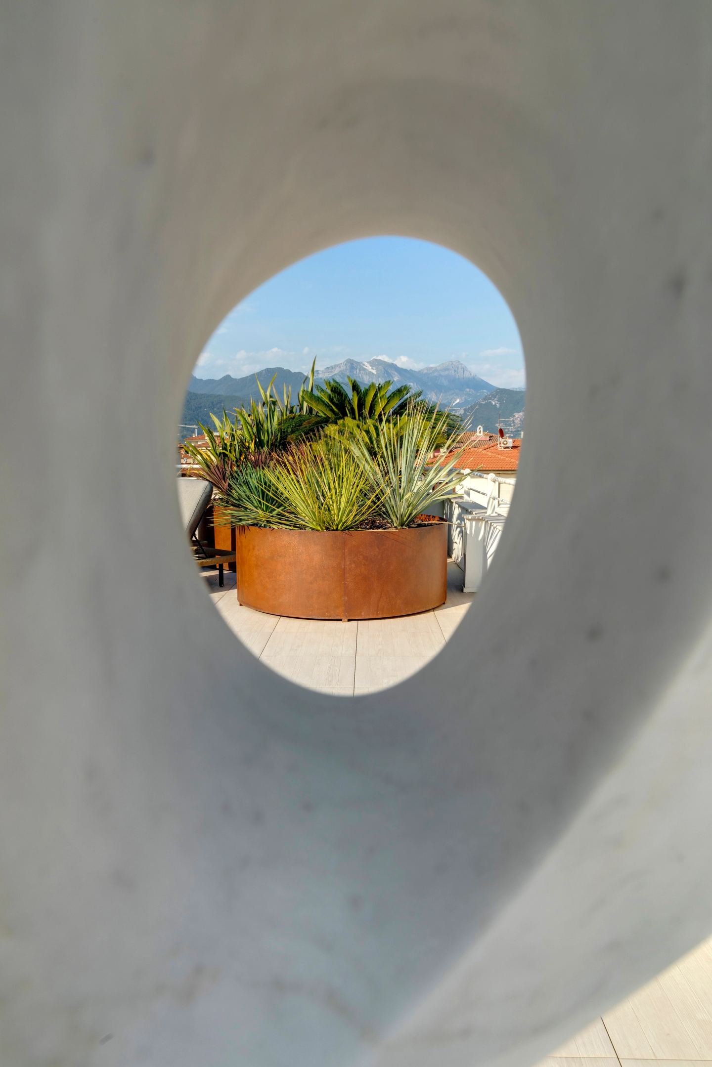 Un'apertura circolare nel parapetto inquadra una fioriera in corten