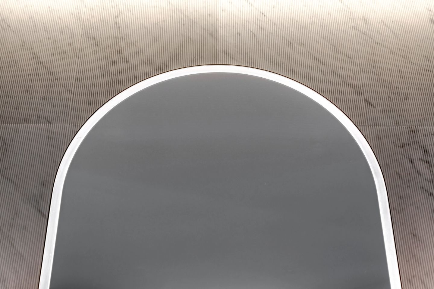 Backlit oval mirror above the fluted marble wall