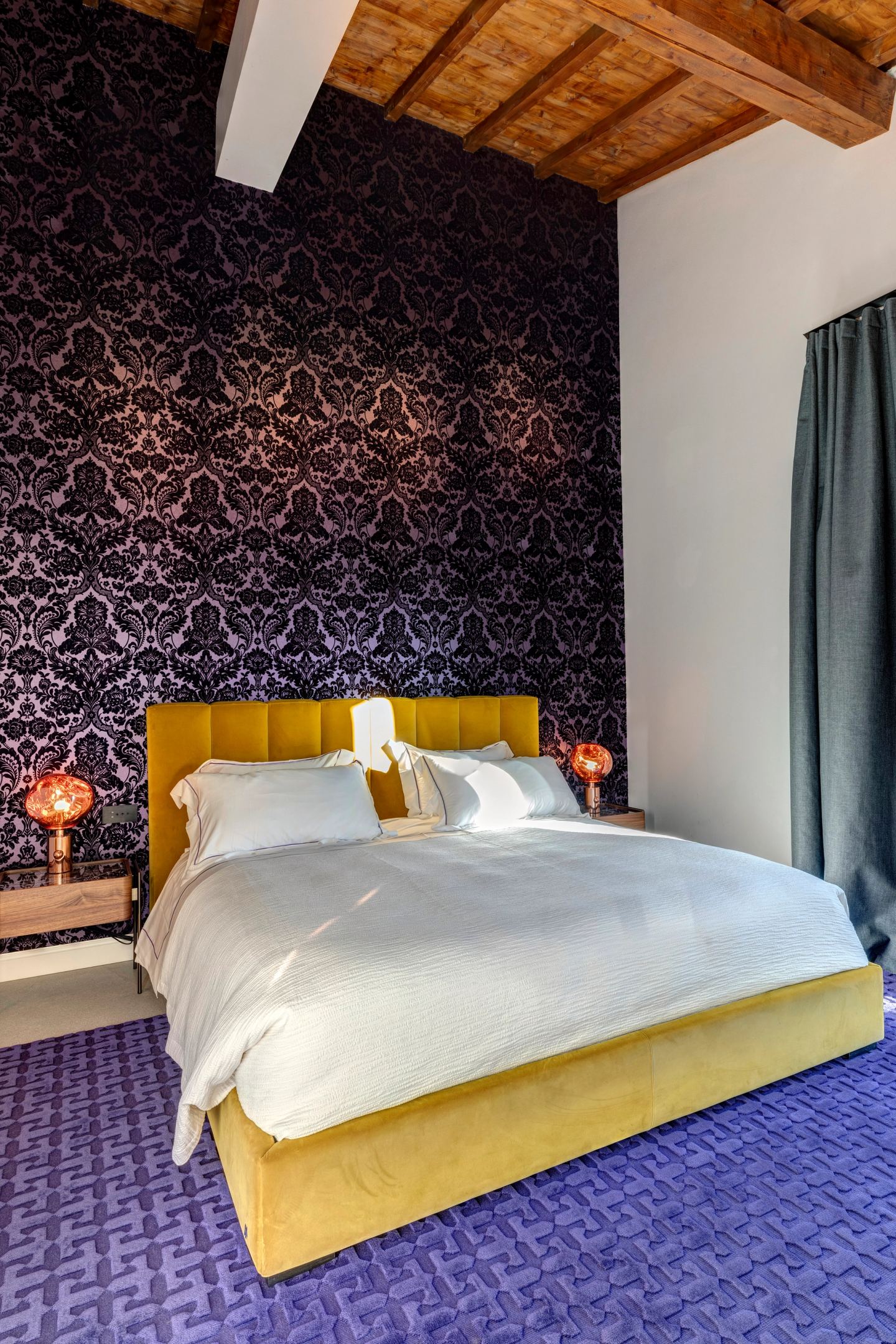 The bed against the damask wall, yellow velvet headboard