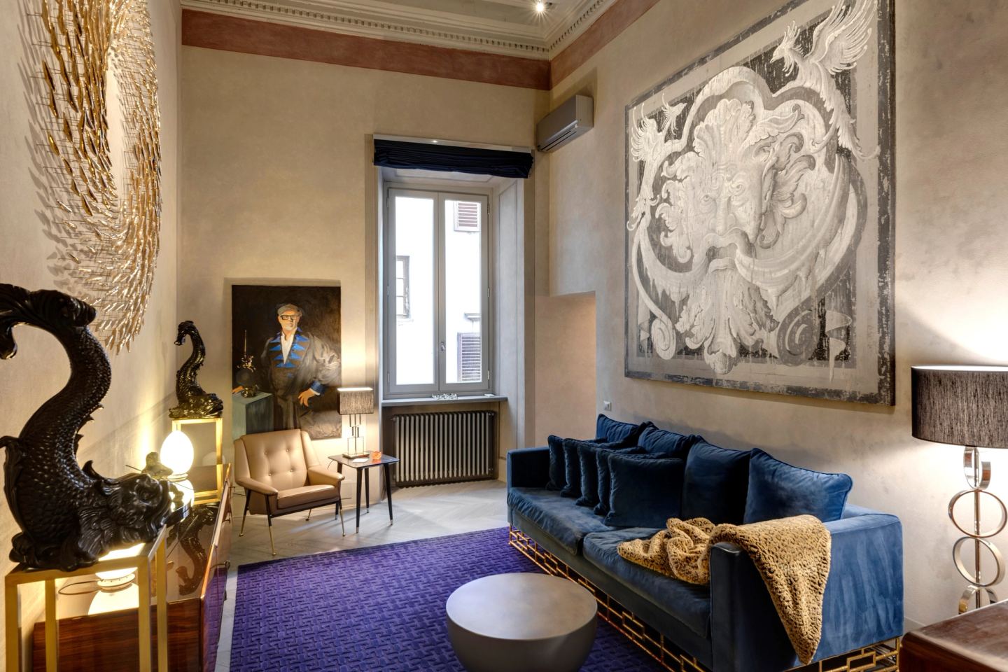 The sitting room: a blue velvet sofa on a violet rug, a large baroque panel above it
