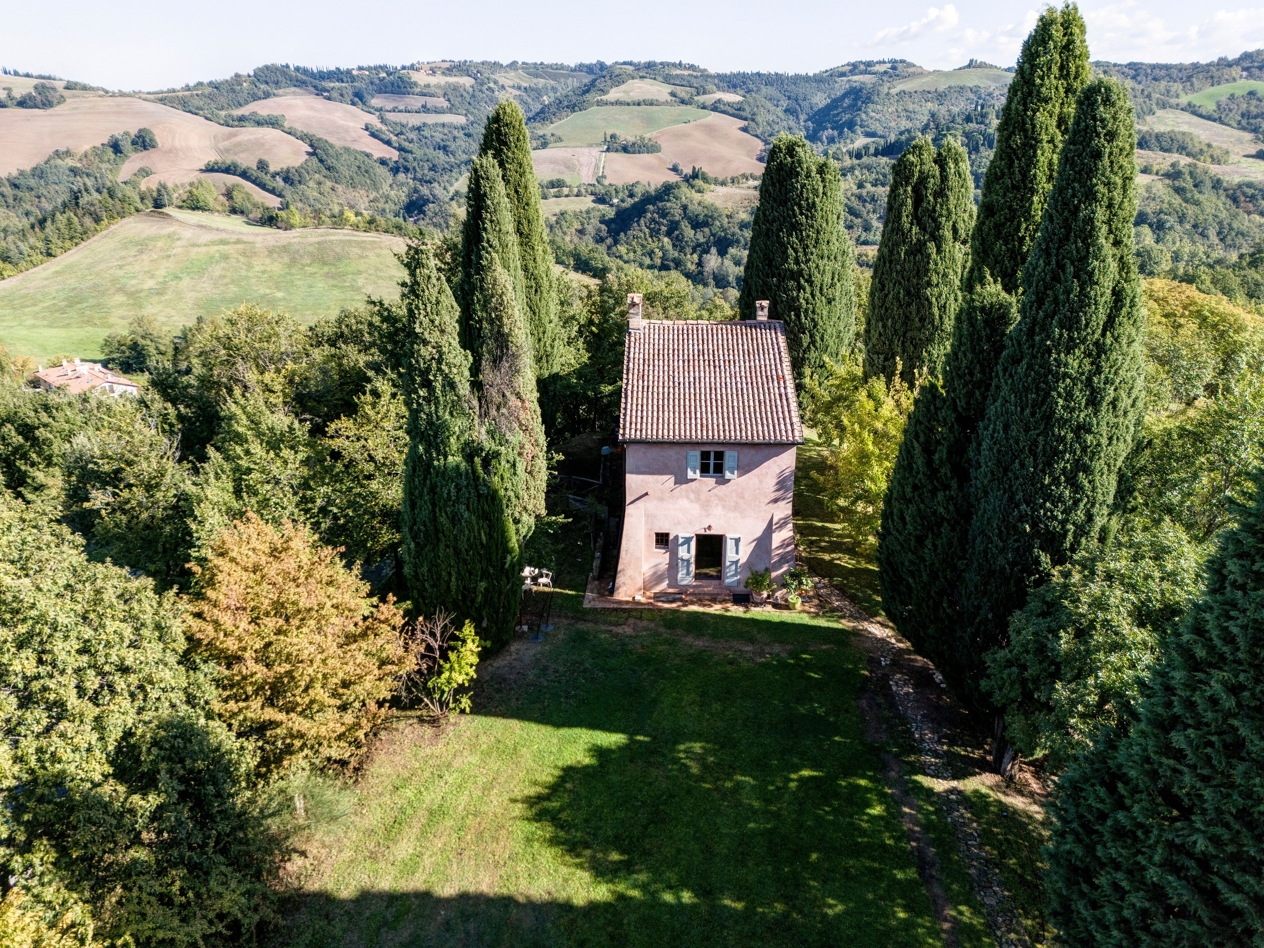 La GuestHouse dall'alto, una casa rosa tra alti cipressi, le colline che si allontanano sullo sfondo