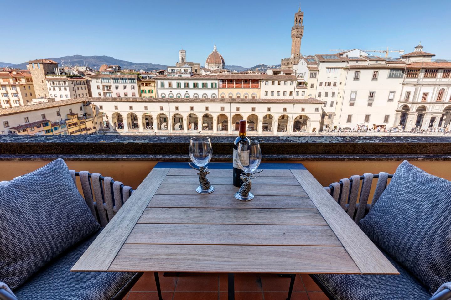 Two glasses on the terrace table, the Uffizi arcade below