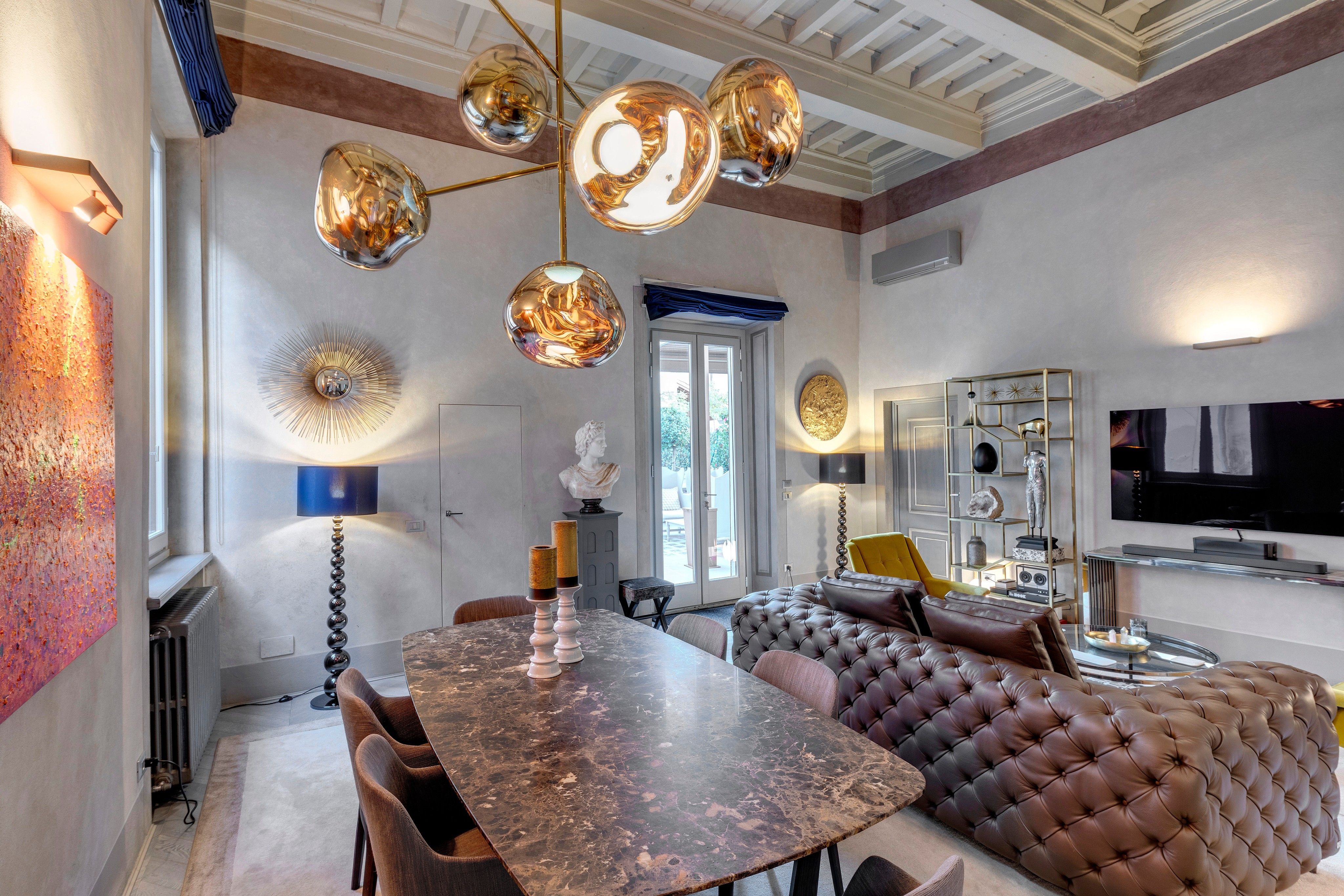 The living and dining room: the gold chandelier over the marble table, the tufted leather sofa beyond