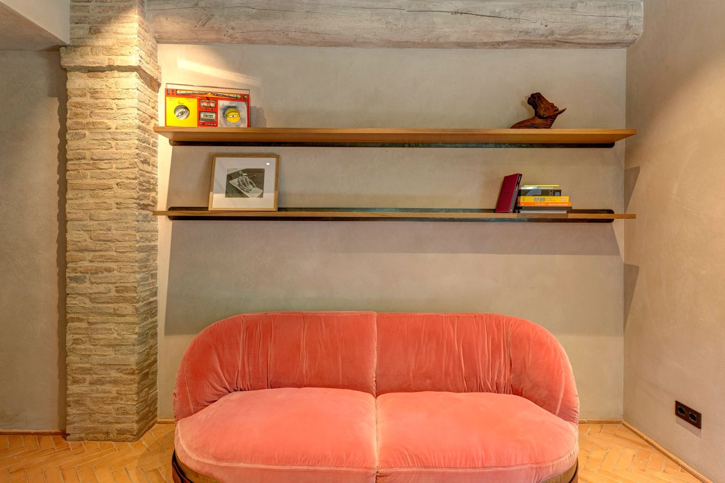 The sofa against the brick, shelves above