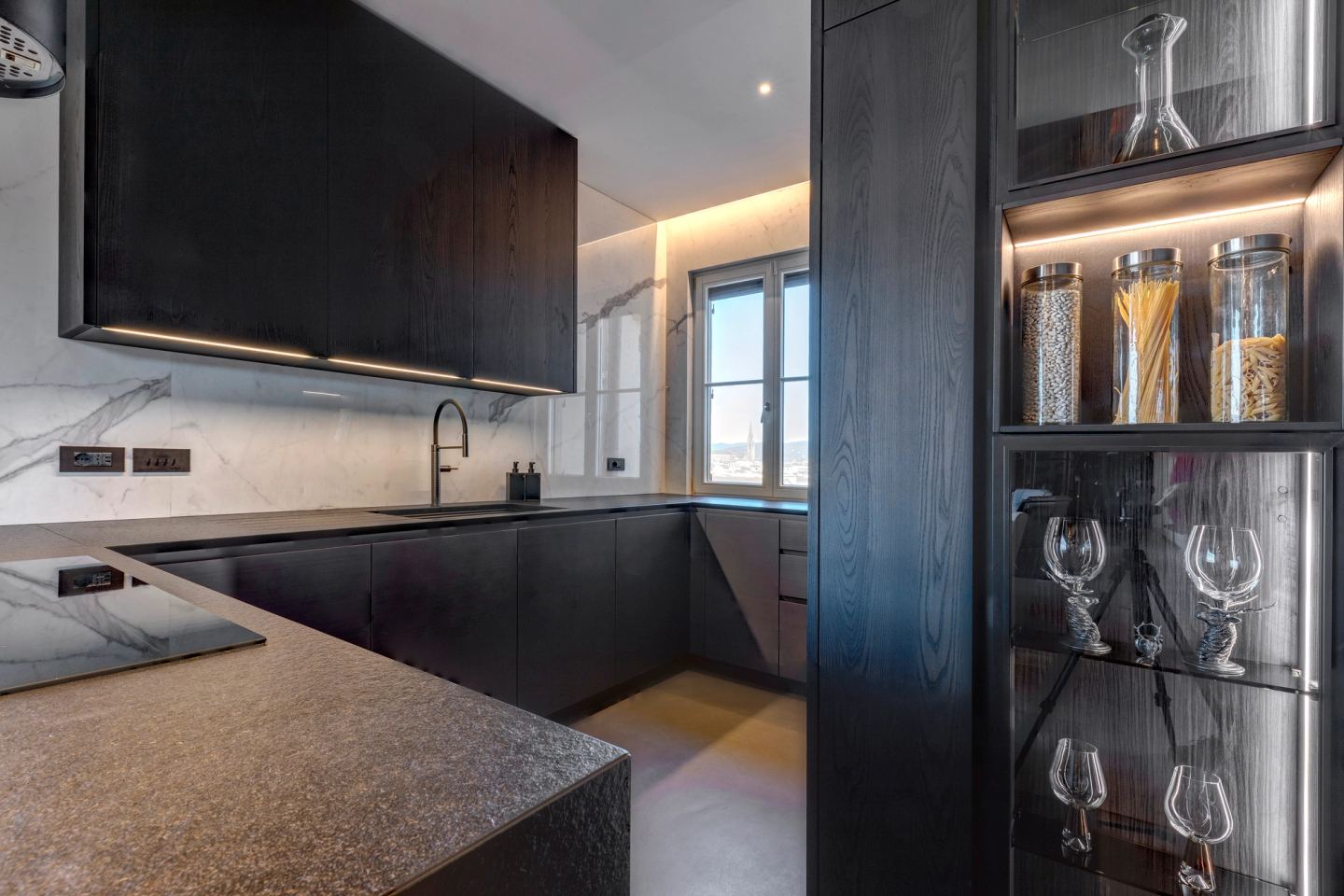 The worktop returning to the window, glassware lit in the cabinet