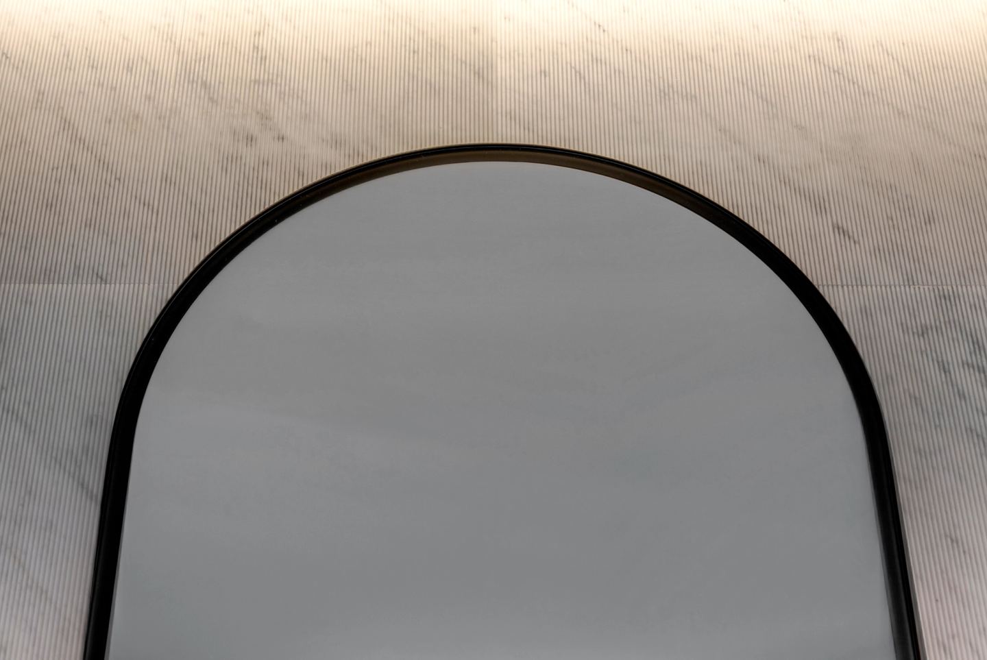 Arched mirror with a slim black frame on veined marble