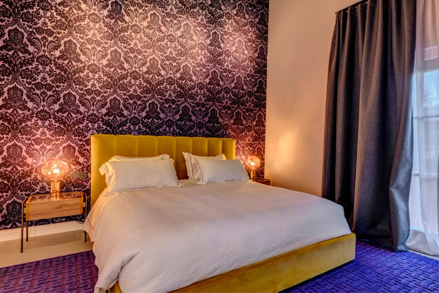 The bed below the beams, damask and purple carpet