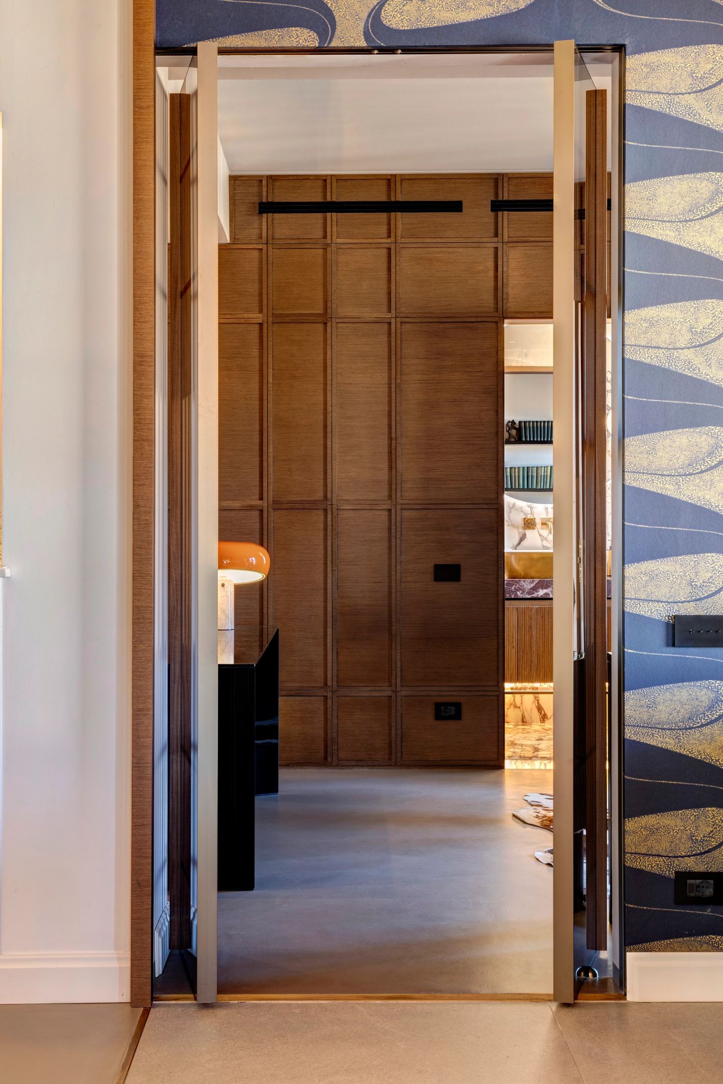 The pivoting slatted door standing open against the patterned wall