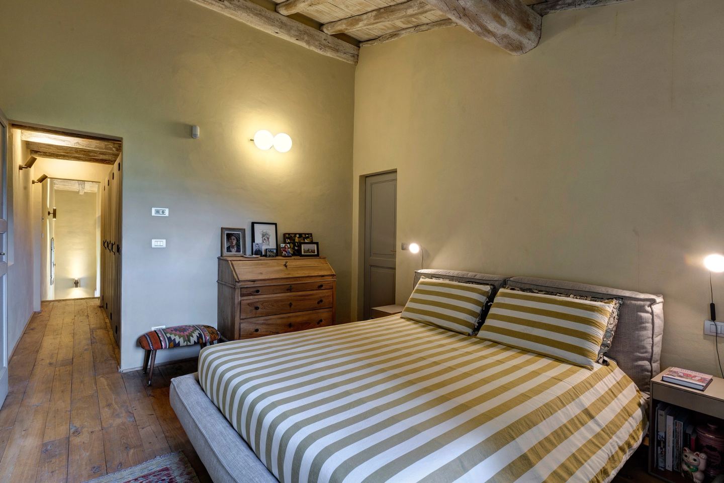 The master bedroom: the upholstered bed in striped linen, the old secretaire behind