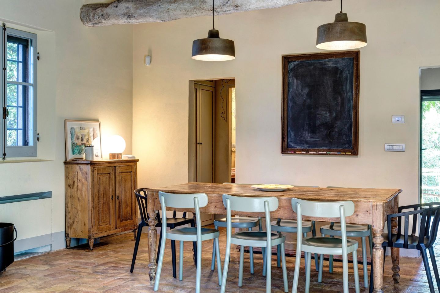 La sala da pranzo: un lungo tavolo in legno sotto due sospensioni scure