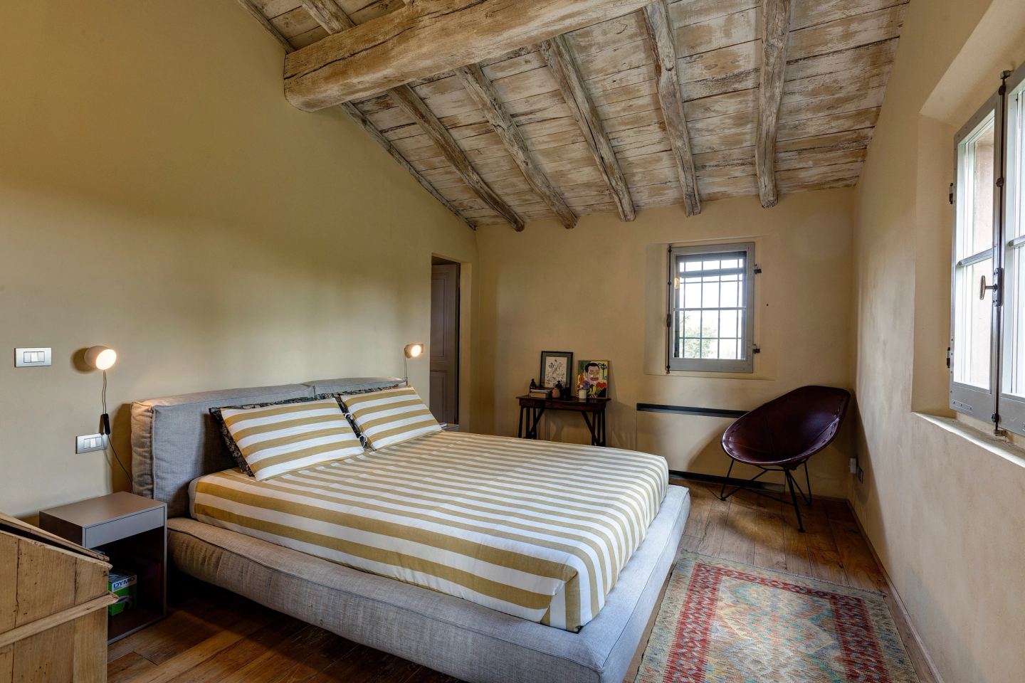 The bed under the beams, the window and a woven chair