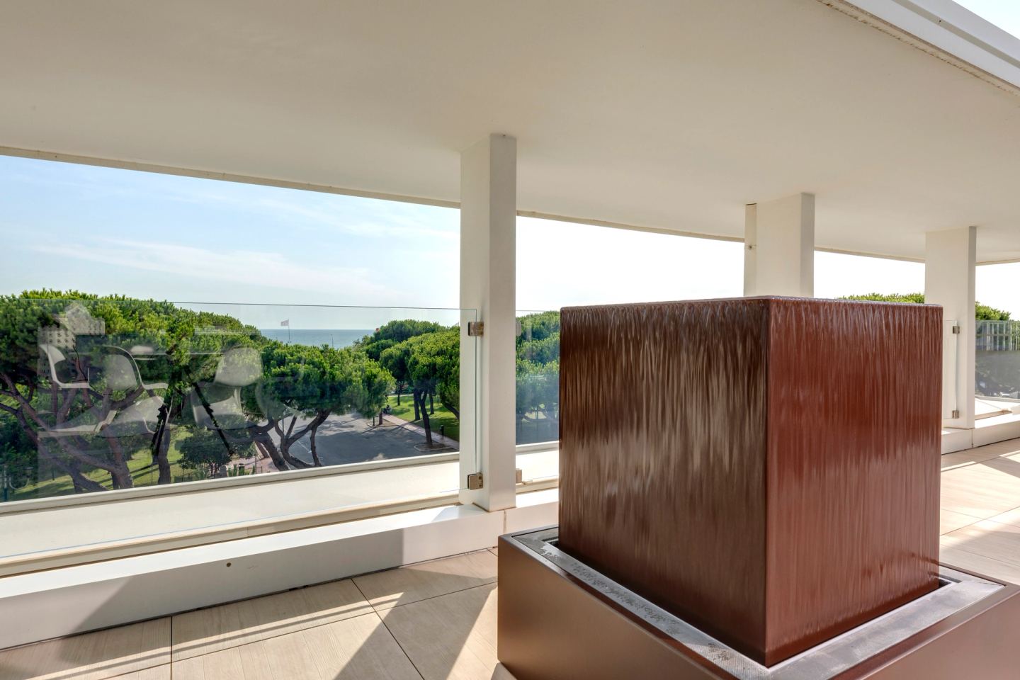 The corten water column, its ribbed face wet, basin at its foot