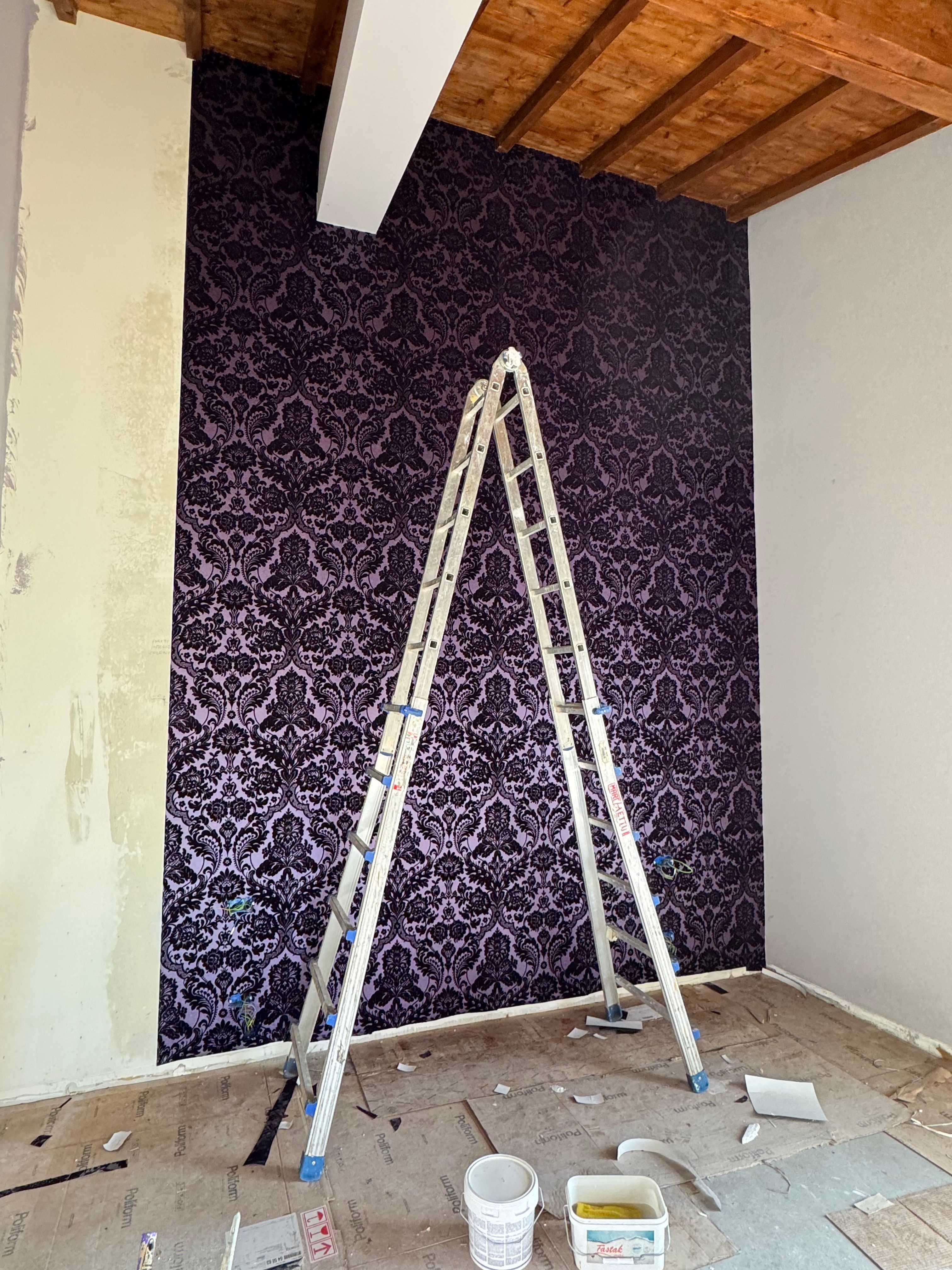 The bedroom's velvet wallpaper, one wall hung, the ladder still up