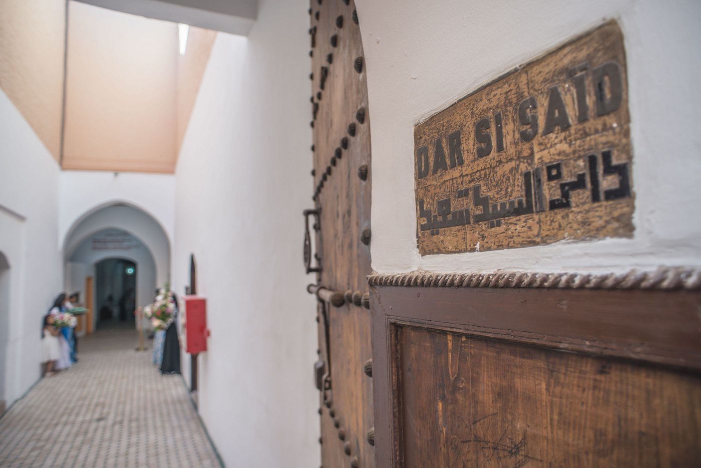 Studded wooden door with carved Dar Si Said sign beside a white museum corridor