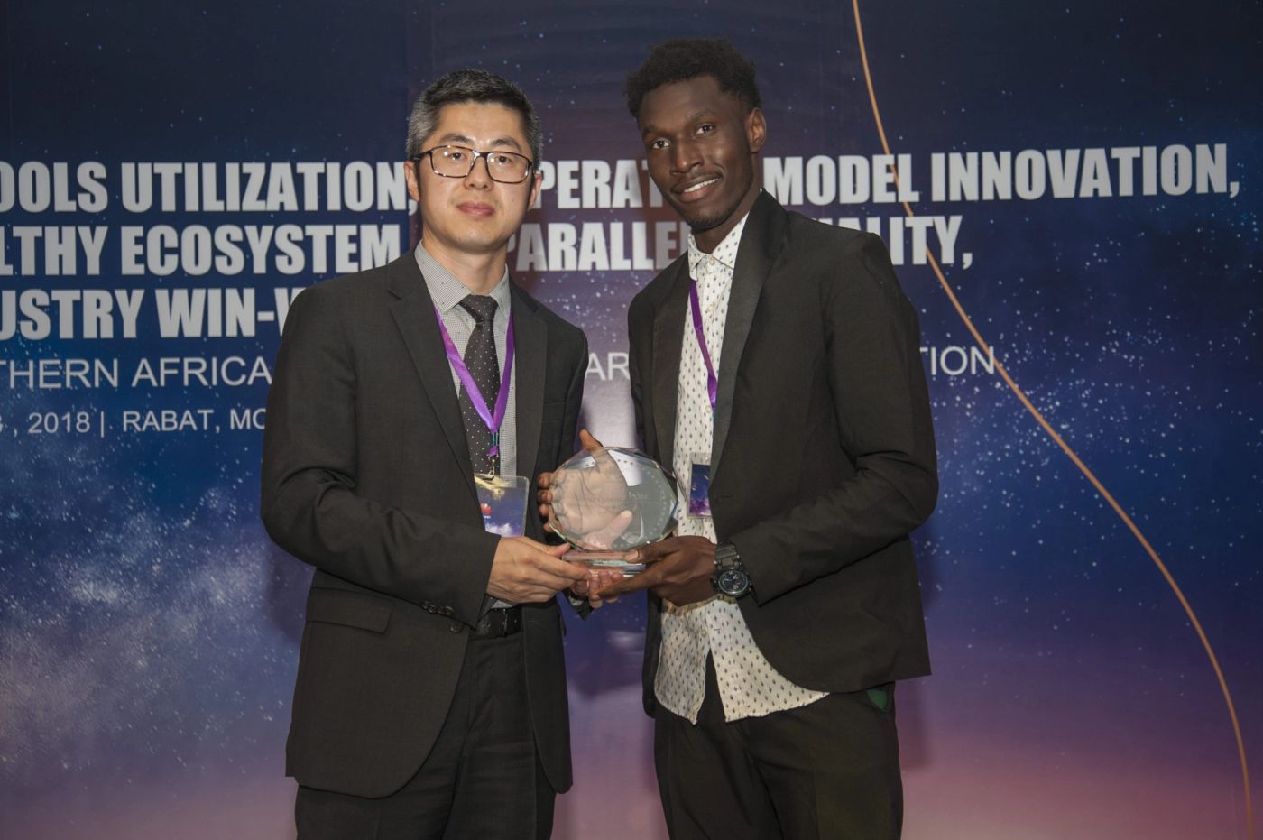 Two men in suits hold a glass trophy together at a Huawei award ceremony in Rabat