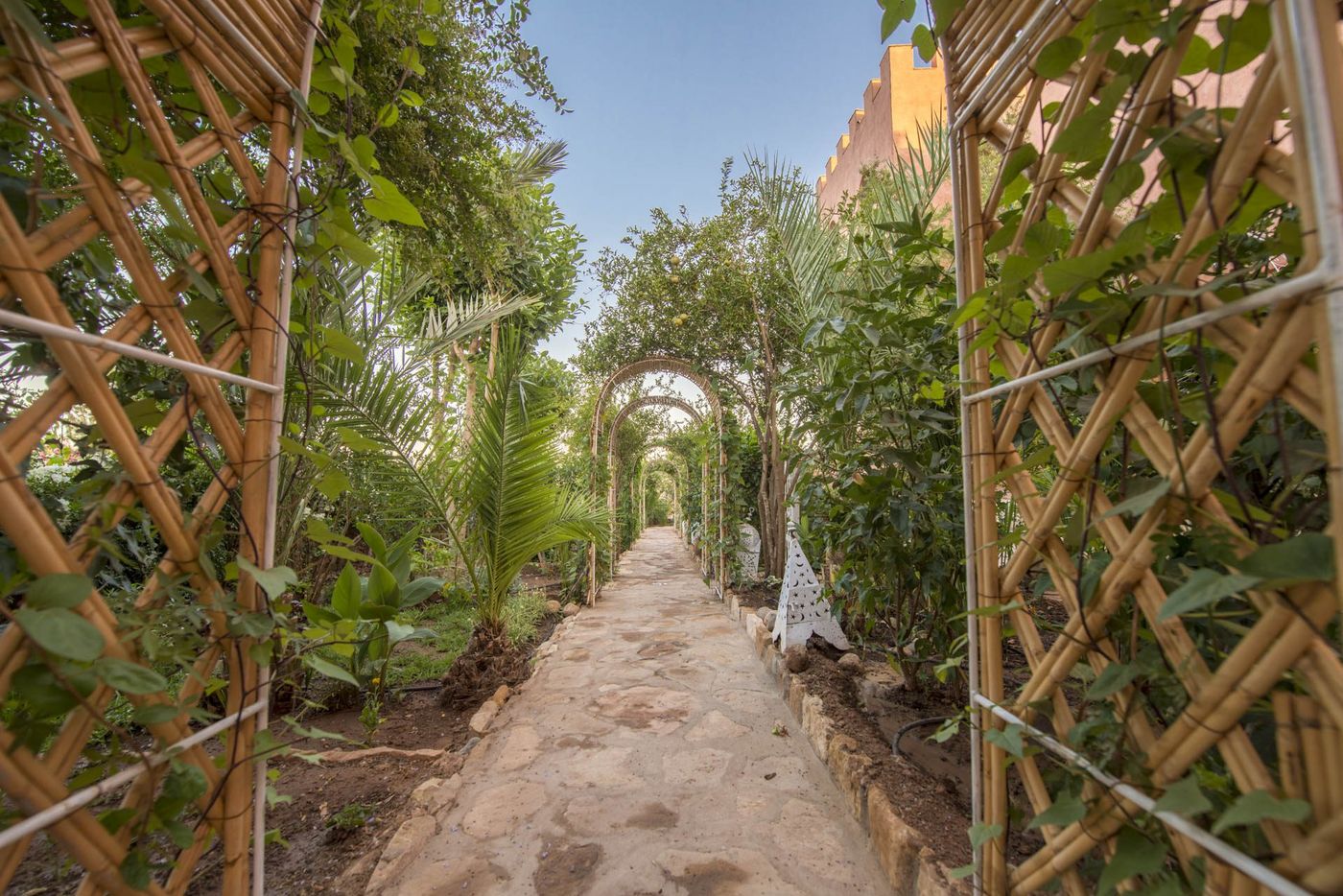 Stone garden path arched with greenery leading toward an earthen kasbah lodge