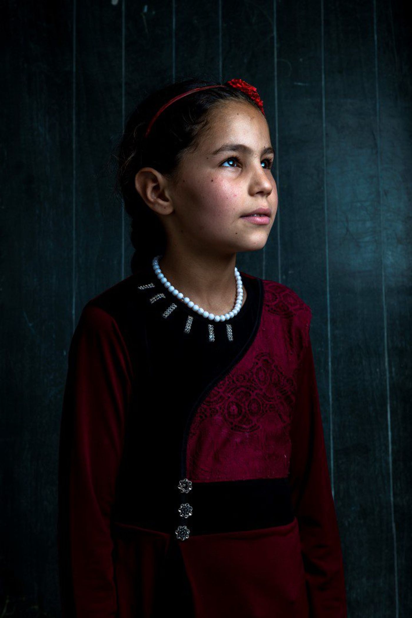 Young girl in a red and black embroidered dress and pearl necklace gazing upward