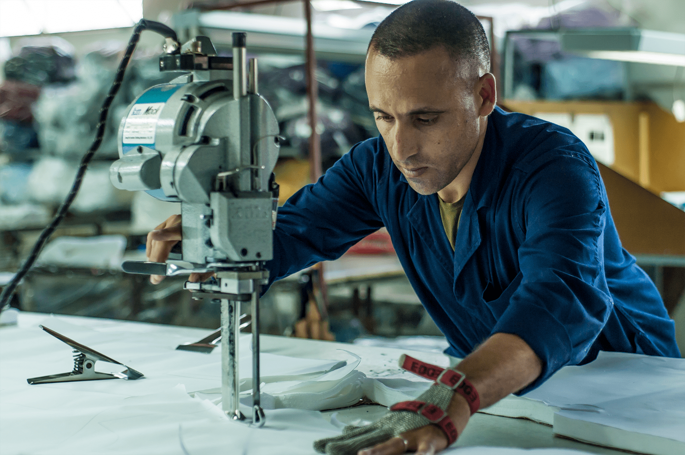 Man in blue overalls cuts white fabric with an industrial cutting machine in a textile workshop