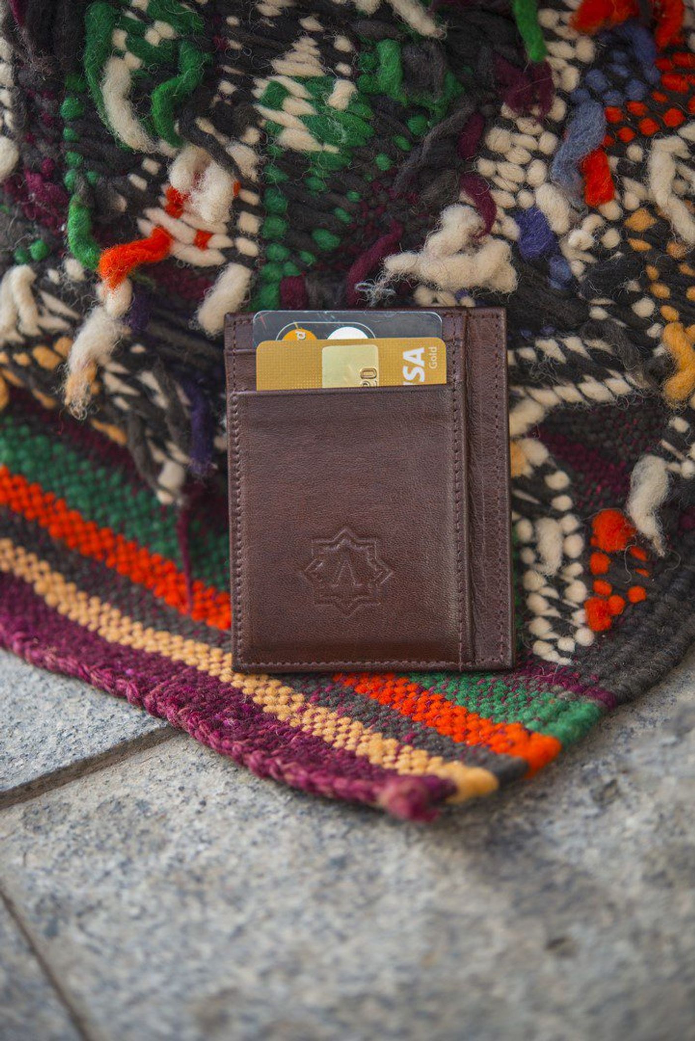Brown leather card wallet holding Visa cards, resting on a fringed Berber rug on stone