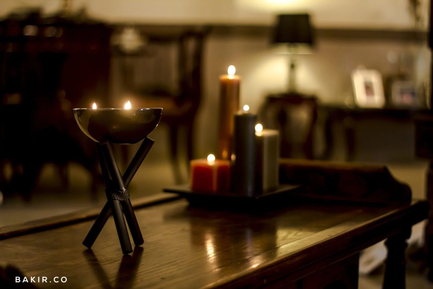 Lit candles on a black tripod holder and tray atop a dark wooden table in a dim room