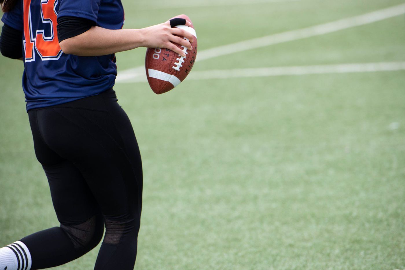 Woman in navy number 13 jersey running with an American football tucked in hand