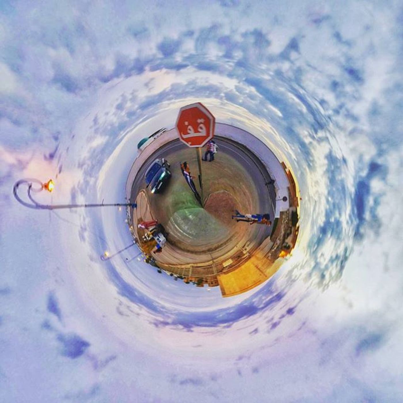 Tiny-planet panorama of a roadside lot with an Arabic stop sign under a vast cloudy sky