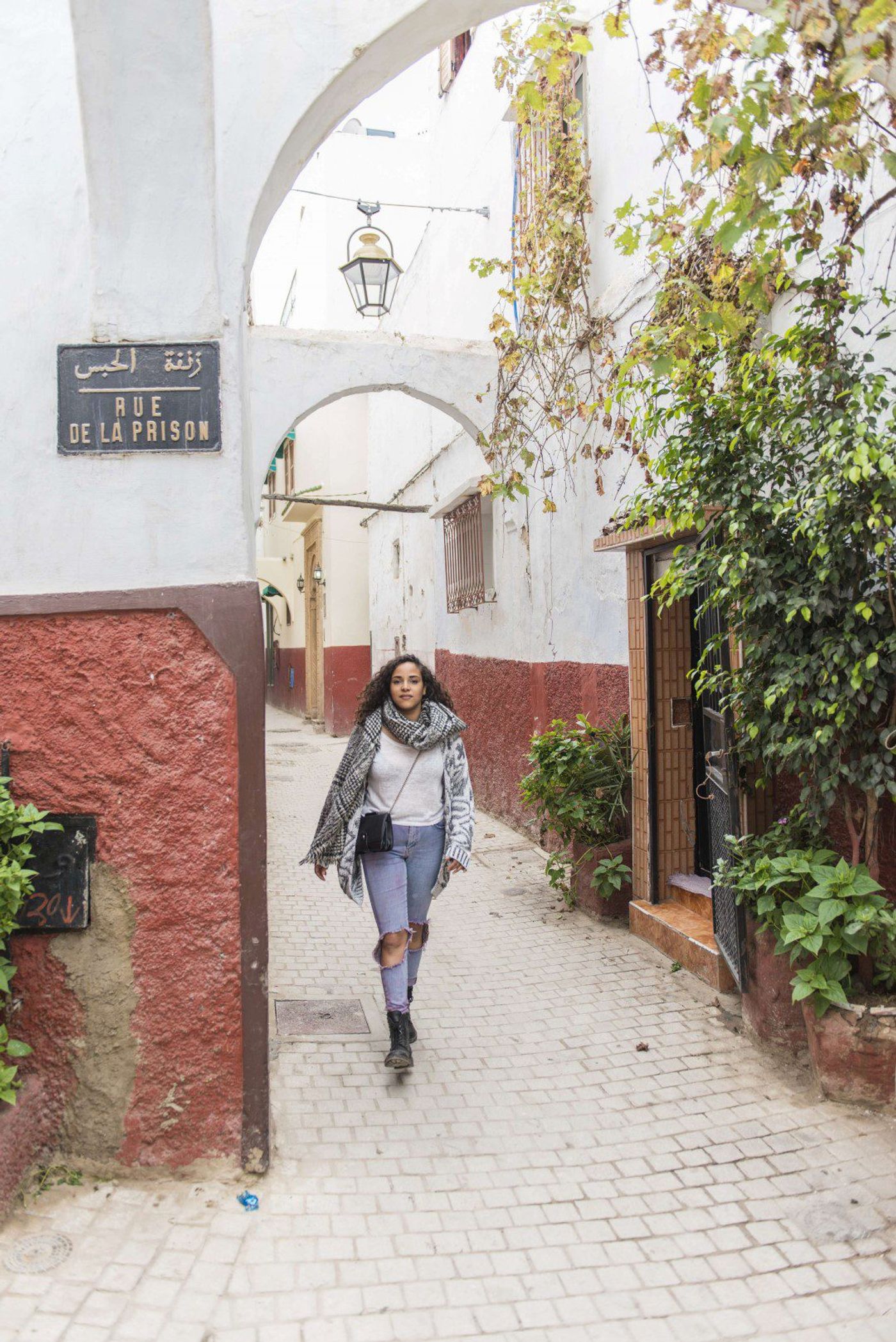 Woman in scarf walks down a narrow Rabat medina alley past a Rue de la Prison sign