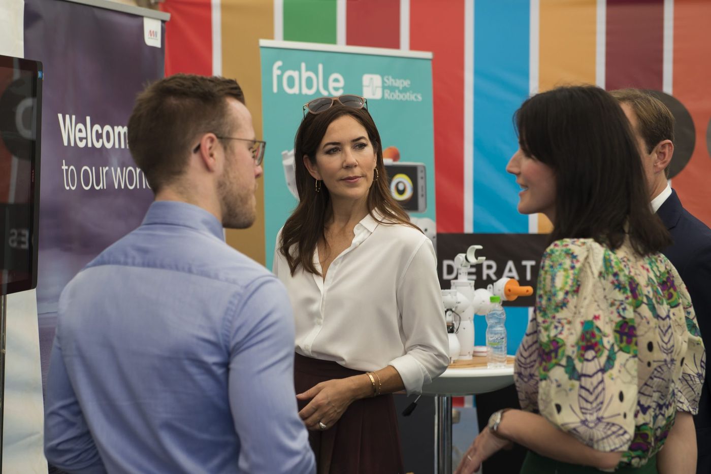 Woman in white blouse talks with two people beside startup banners at an innovation summit