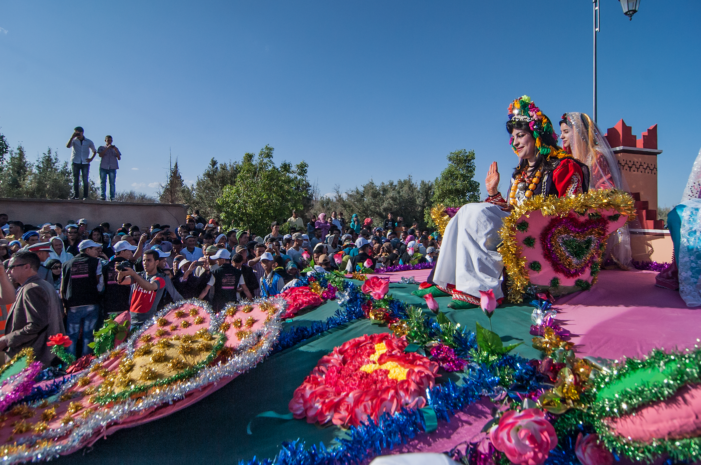 Women in Berber dress wave from a flower-decked parade float before a crowd