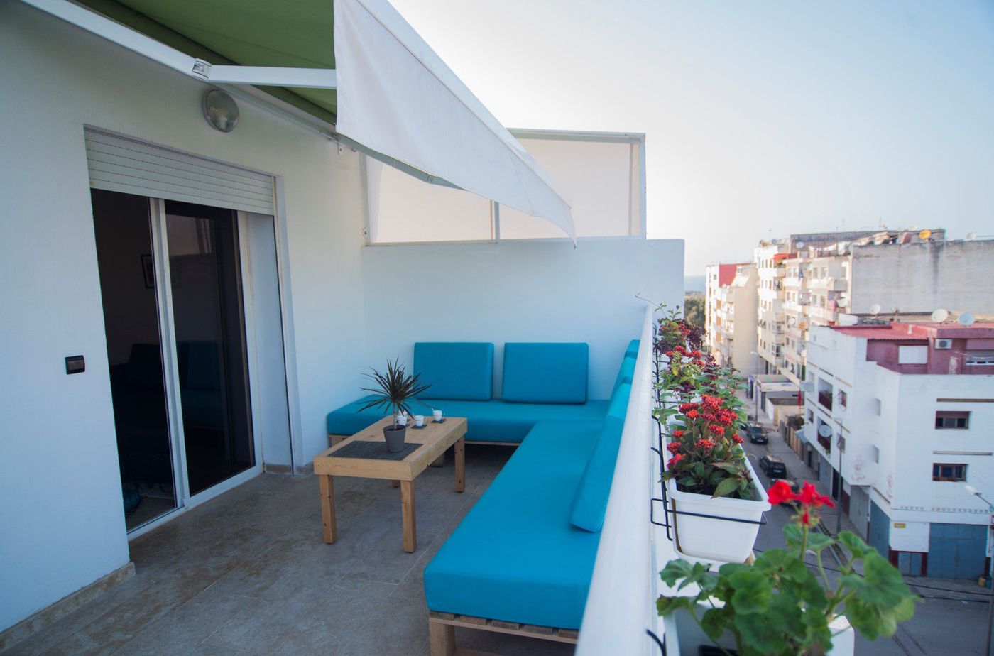 Rooftop terrace with turquoise sofas and a low table overlooking a sunlit city street