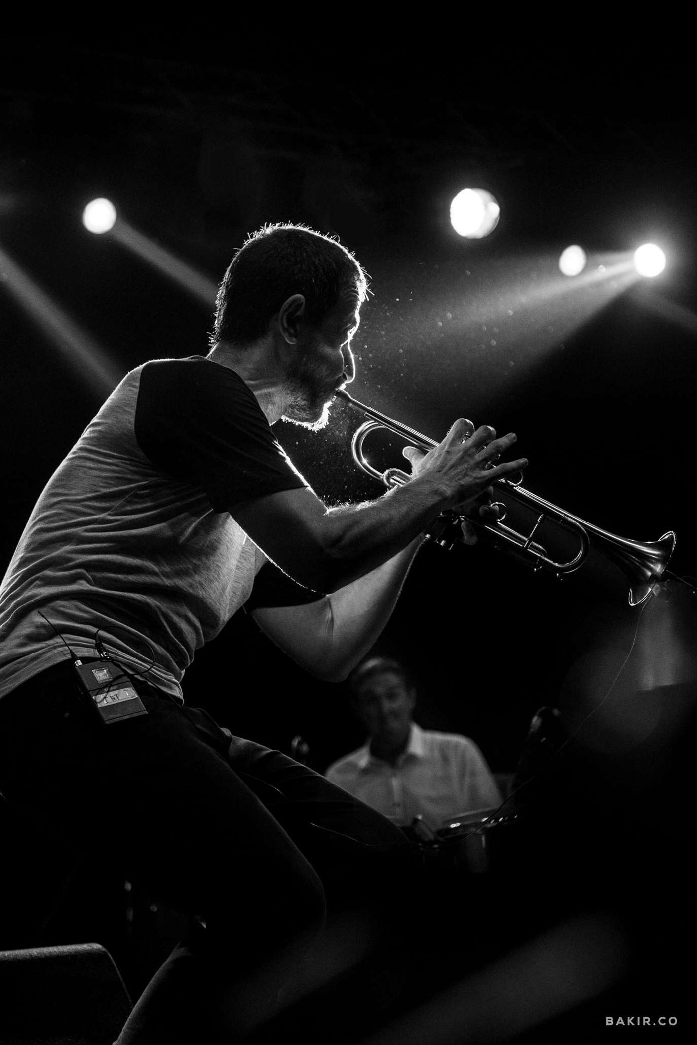 Trumpeter leans back blowing hard under stage spotlights, breath spray visible, jazz performance in black and white