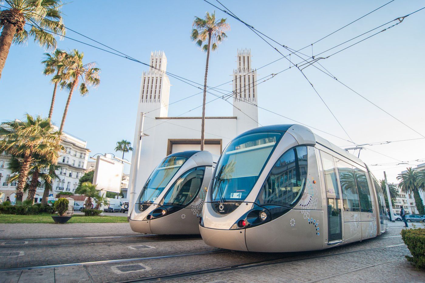 Two sleek silver trams parked on tracks before a white modernist church with twin towers