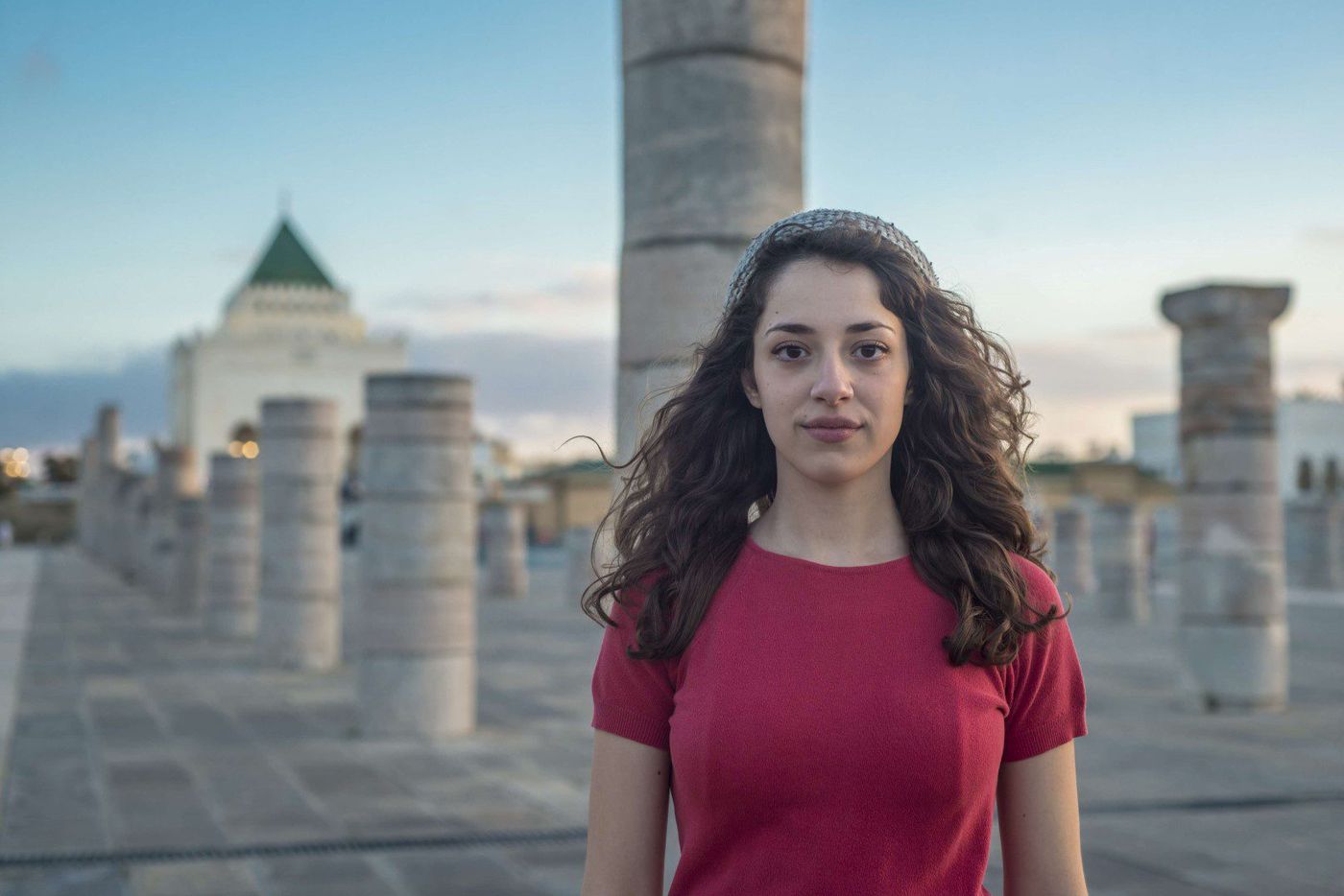 Curly-haired woman in red top stands among the columns of the Mausoleum esplanade in Rabat