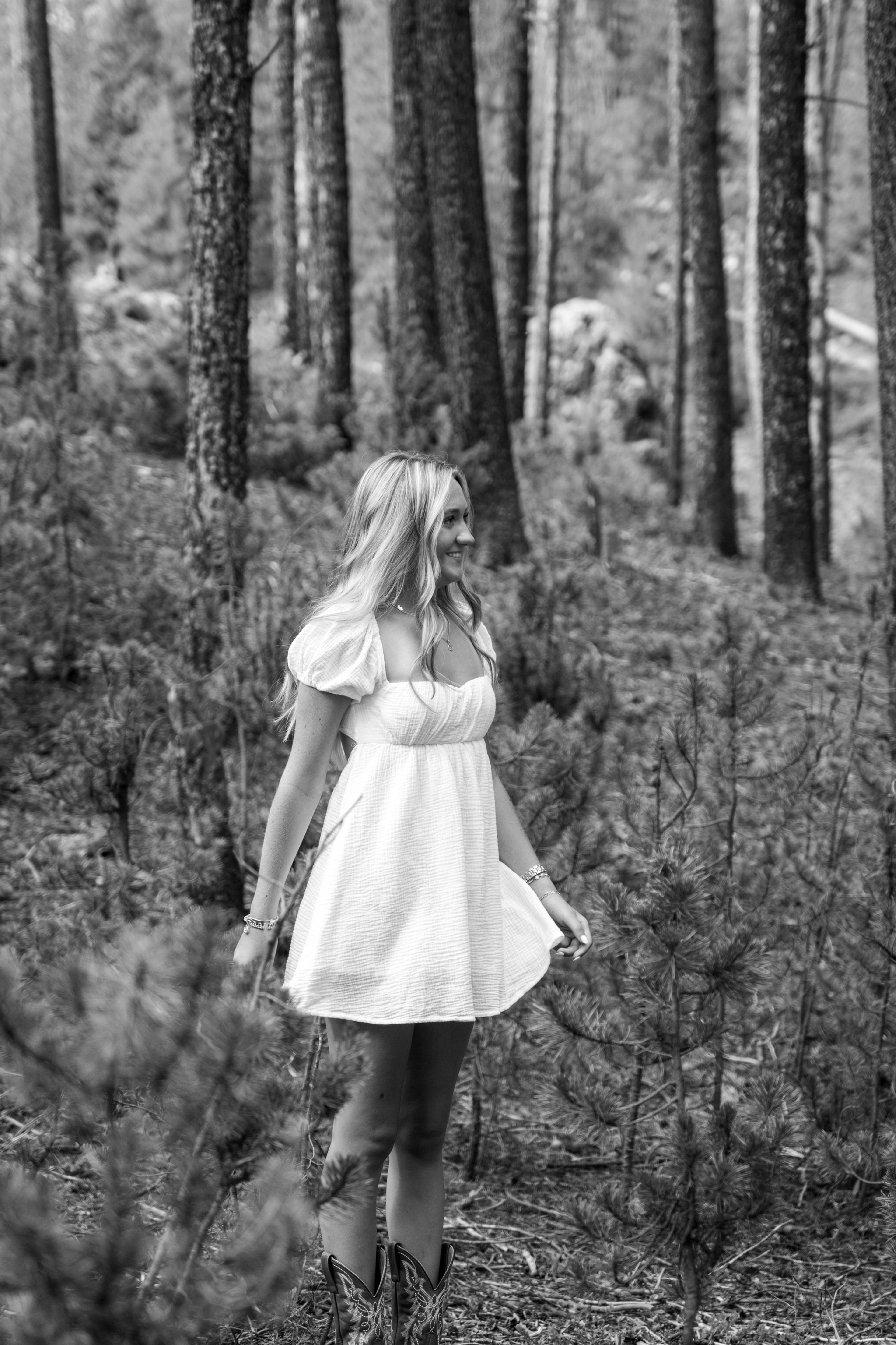 Black-and-white portrait of Caleigh turning in a pine forest