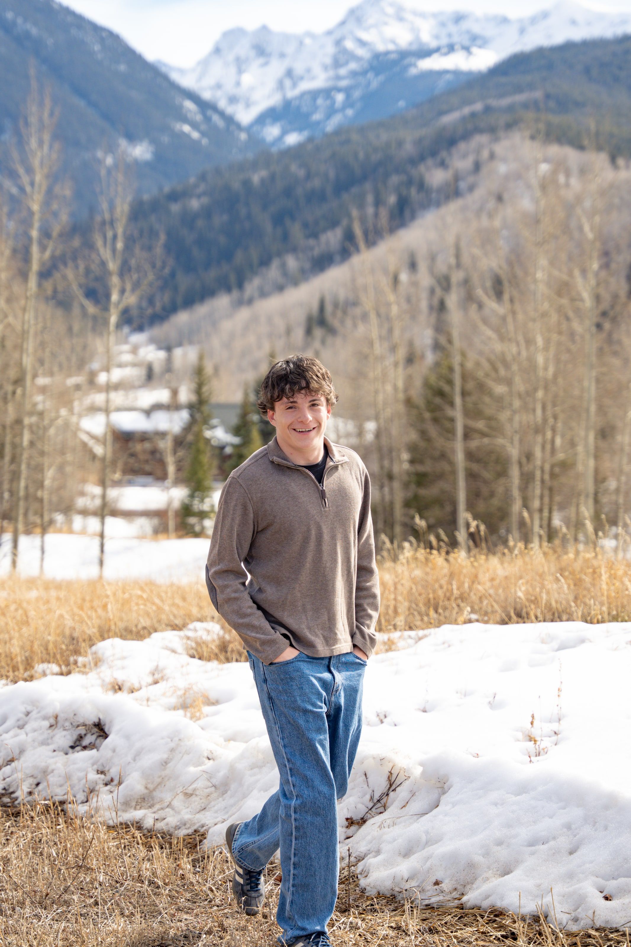 Luca in a brown sweater standing in a snowy meadow below the peaks