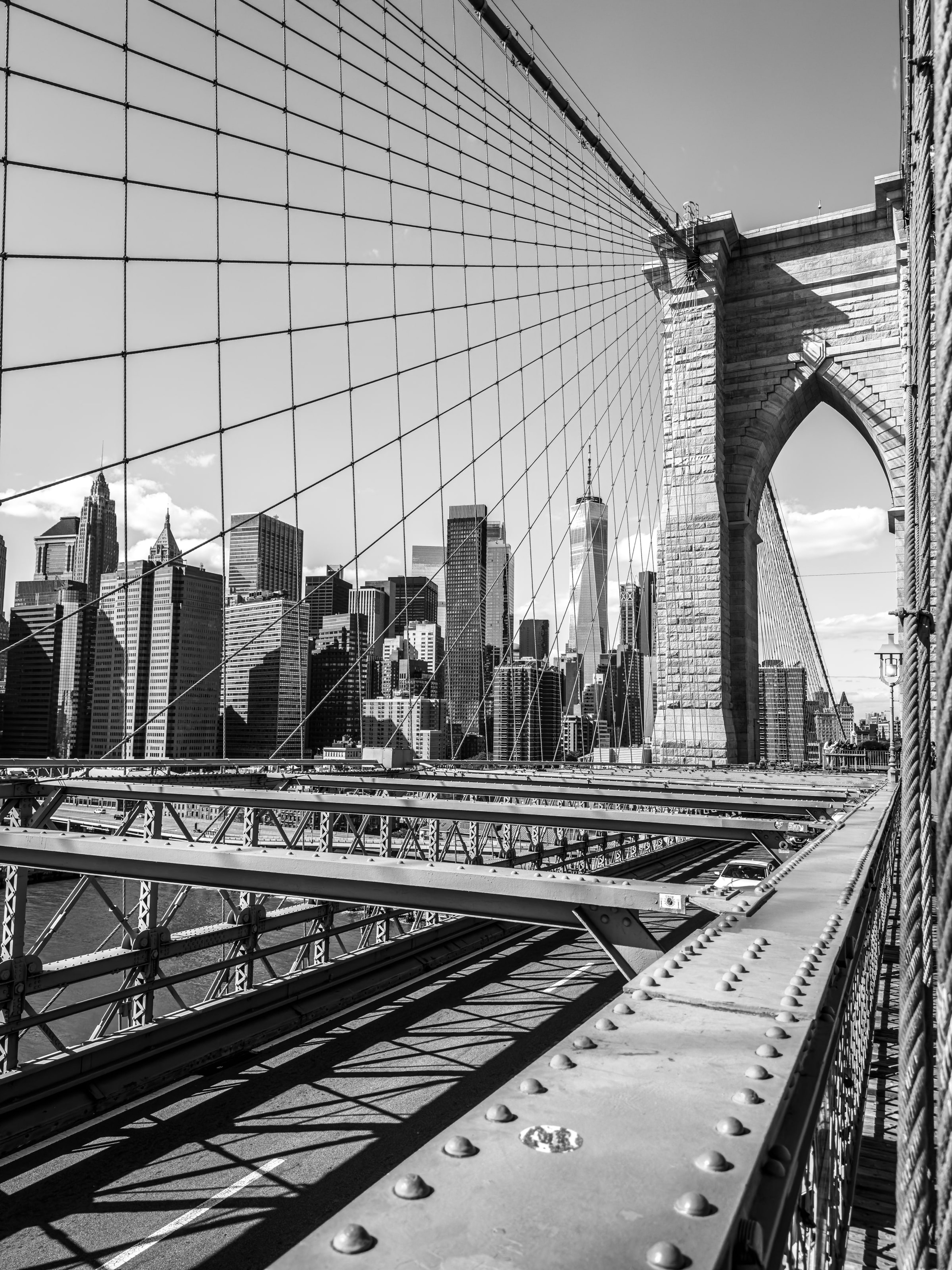 Brooklyn Bridge cables radiating over the walkway with the Manhattan skyline beyond, in black and white
